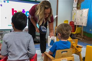A teacher showing an image of a backpack to a preschool student.